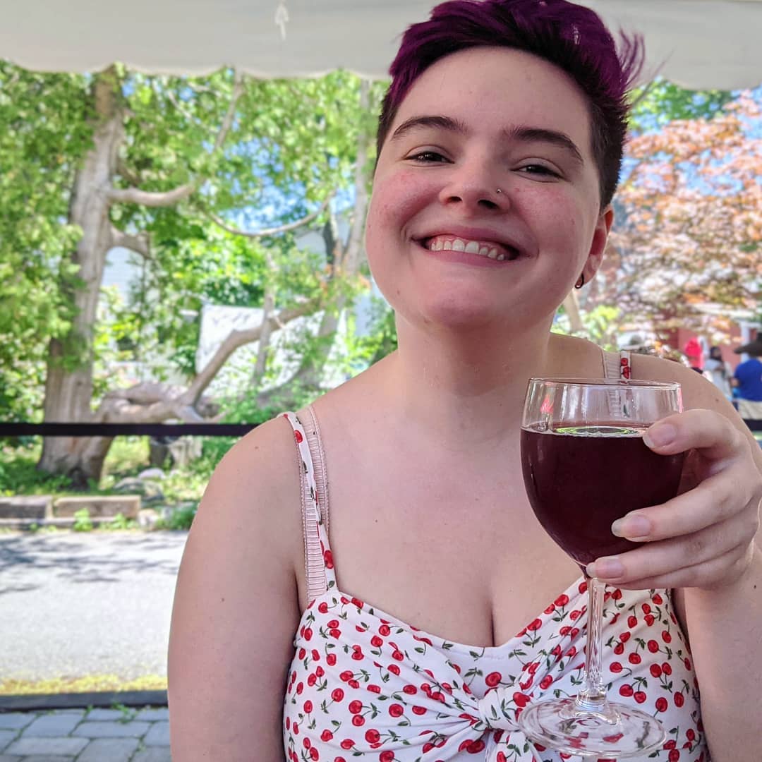 picture of me (Hannah) with short hair, smiling and holding a drink